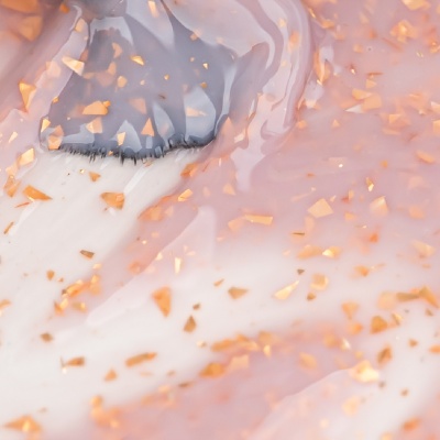 Pincel com cerdas pretas aplicado em superfície cor-de-rosa brilhante com partículas douradas.