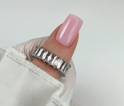 anel prateado com pedras transparentes retangulares num dedo de unha rosa claro