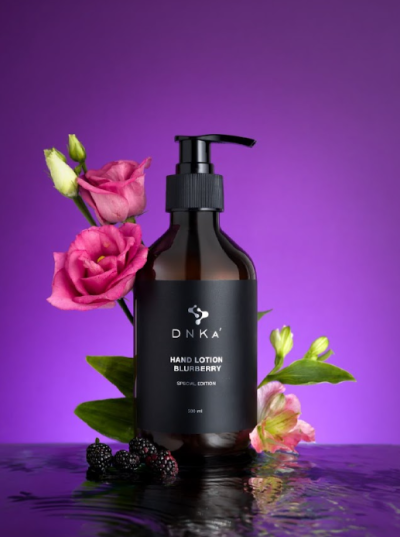 Frasco de loção para mãos DNKA com flores e amoras em fundo roxo