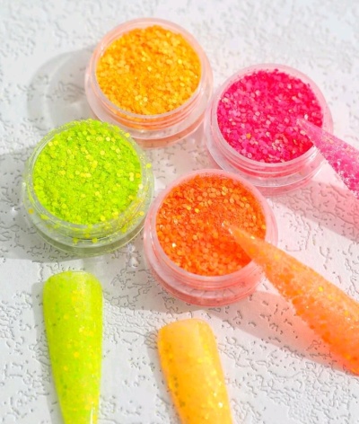 Quatro potes de glitter colorido com amostras de unhas postiças e pincéis aplicadores