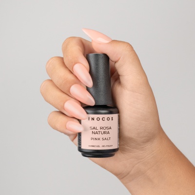 Mão com unhas pintadas segurando frasco de verniz gel INOCOS Sal Rosa Natura