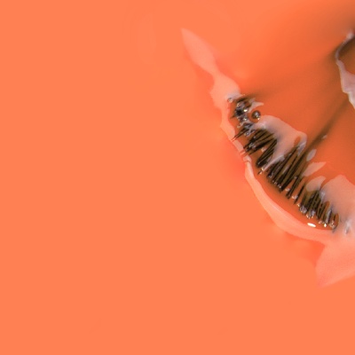 Frasco de vidro transparente com tampa preta e objetos metálicos em fundo laranja