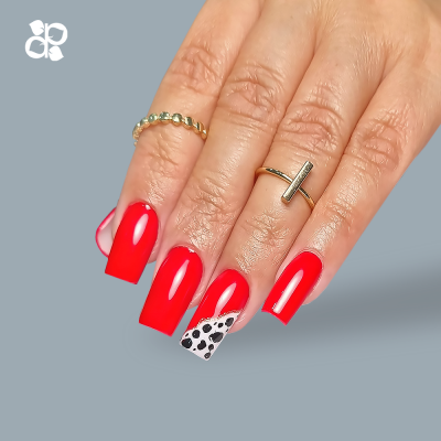 Unhas vermelhas brilhantes com padrão em bolinhas no anelar e dois anéis dourados na mão feminina