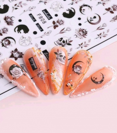 Unhas postiças laranja decoradas com flores, caveiras e detalhes em strass