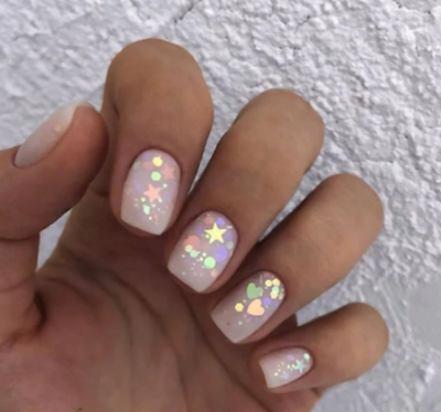Unhas com verniz nude claro e decoração holográfica de corações e estrelas