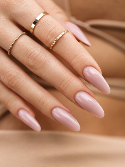 Mão feminina com unhas longas cor rosa claro e anéis dourados