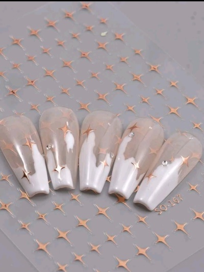 Unhas postiças transparentes e brancas com estrelas douradas e cristais sobre fundo cinza