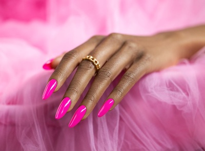 Mão com unhas rosa vibrante e anel dourado sobre tecido rosa