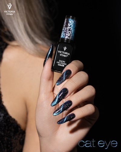 Mão feminina com unhas longas pintadas com verniz gel cat eye preto azulado segurando frasco de verniz VICTORIA VYNN
