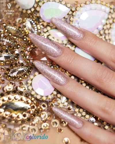 Unhas longas com verniz rosa brilhante sobre superfície decorada com pedrarias douradas e iridescentes