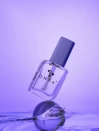 Frasco de verniz para unhas DNKA com tampa azul sobre superfície de água lilás
