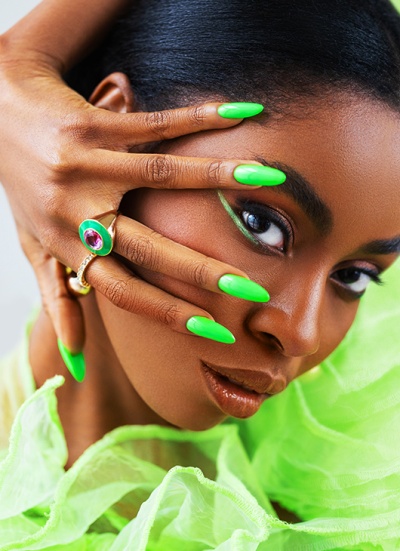 Close-up de mulher com unhas verdes, maquiagem verde e anéis dourados