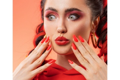 Mulher com maquilhagem vermelha e unhas vermelhas brilhantes em fundo laranja