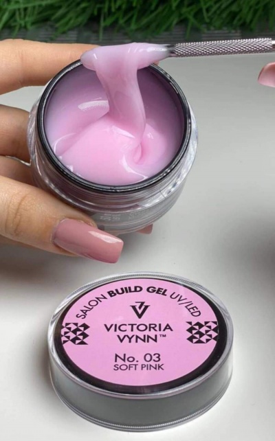 Gel de construção para unhas rosa suave em frasco aberto com tampa ao lado.