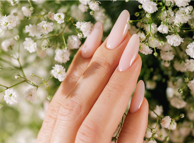 Mão com unhas nude brilhosas e flores brancas delicadas ao fundo