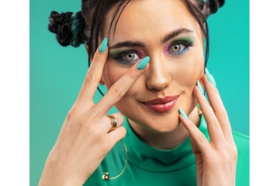 Mulher com unhas azuis, maquilhagem colorida e roupa verde com fundo verde-turquesa