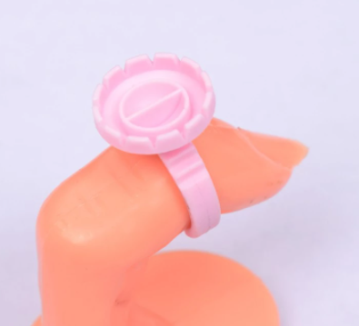 Anel plástico rosa com desenho de cápsula num dedo de manequim laranja