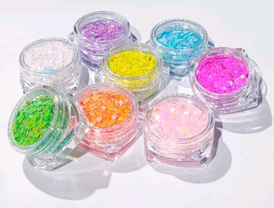 Sete frascos pequenos com glitter colorido variados sobre superfície branca