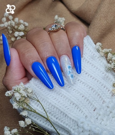 Unhas compridas azul vibrante e com decoração floral em fundo de malha branca e flores secas