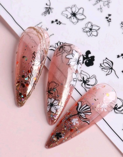 Unhas postiças decoradas com glitter e flores sobre papel com desenhos florais