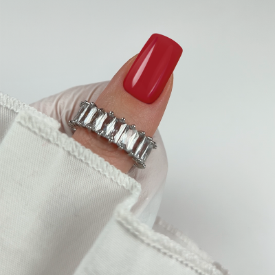 Anel prateado com pedras retangulares em dedo com unha vermelha.