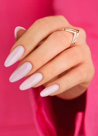Mão com unhas pintadas de rosa claro e anel dourado em fundo rosa