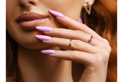 Mão feminina com unhas lilás, anéis dourados e brinco geométrico