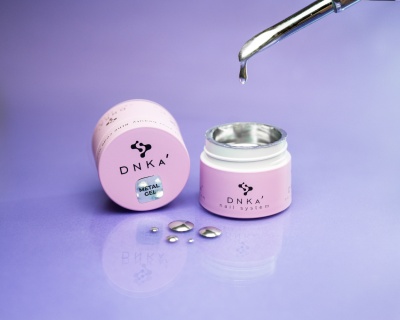 Frasco rosa claro com creme metálico aberto e conta-gotas numa superfície lilás