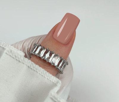 Anel de prata com pedras transparentes retangulares no dedo indicador com unha rosa claro e manga branca.