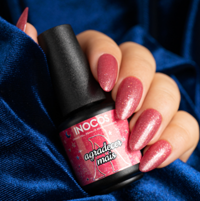 Frasco de verniz INOCOS rosa e unhas pintadas na mão sobre tecido azul