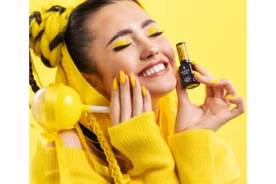 Mulher sorrindo com maquilhagem amarela segurando frasco de verniz de unhas Victoria Vynn