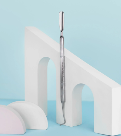 Instrumento metálico para cuidado dental com duas pontas, sobre estrutura branca com arcos, fundo azul claro