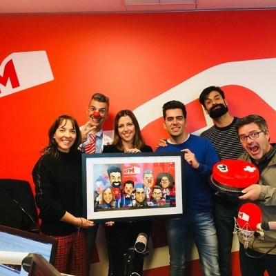 Equipa RFM Grupo de seis pessoas num estúdio de rádio com logo RFM, segurando quadro e objeto vermelho com rosto desenhado