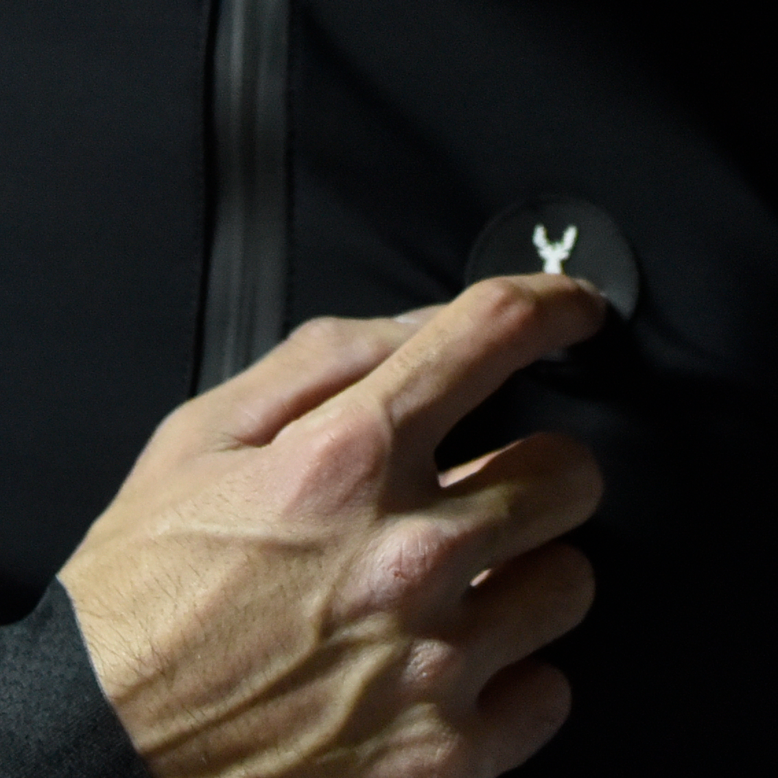 Casaco Ciclismo Led by OSRAM Mão a tocar botão com símbolo de veado em roupa preta