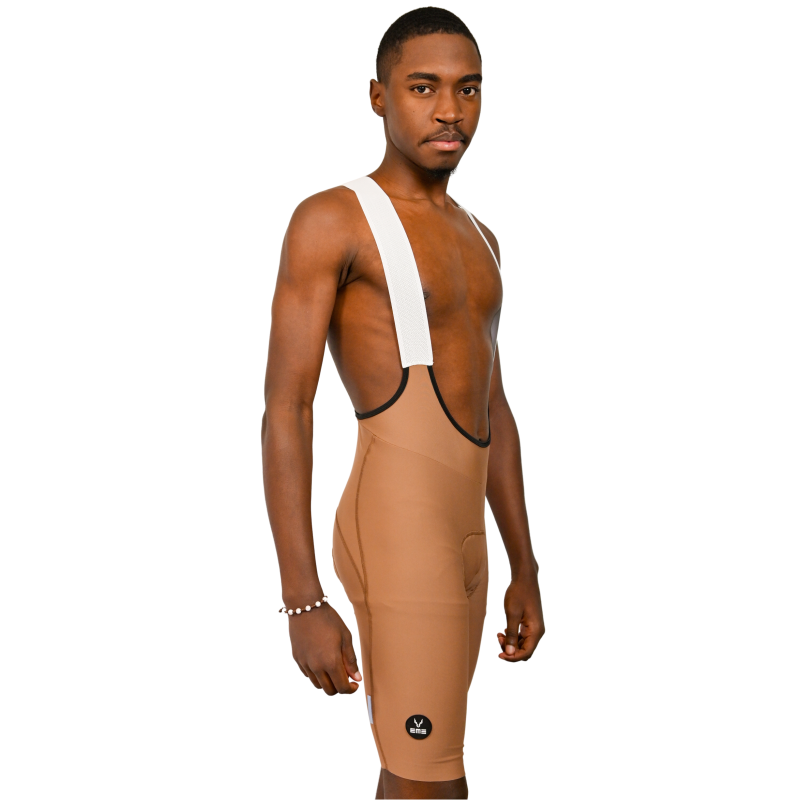 Calções ciclismo Pro Fit Creme Homem a usar calções de ciclismo castanhos com tirantes brancos e logotipo preto na perna.