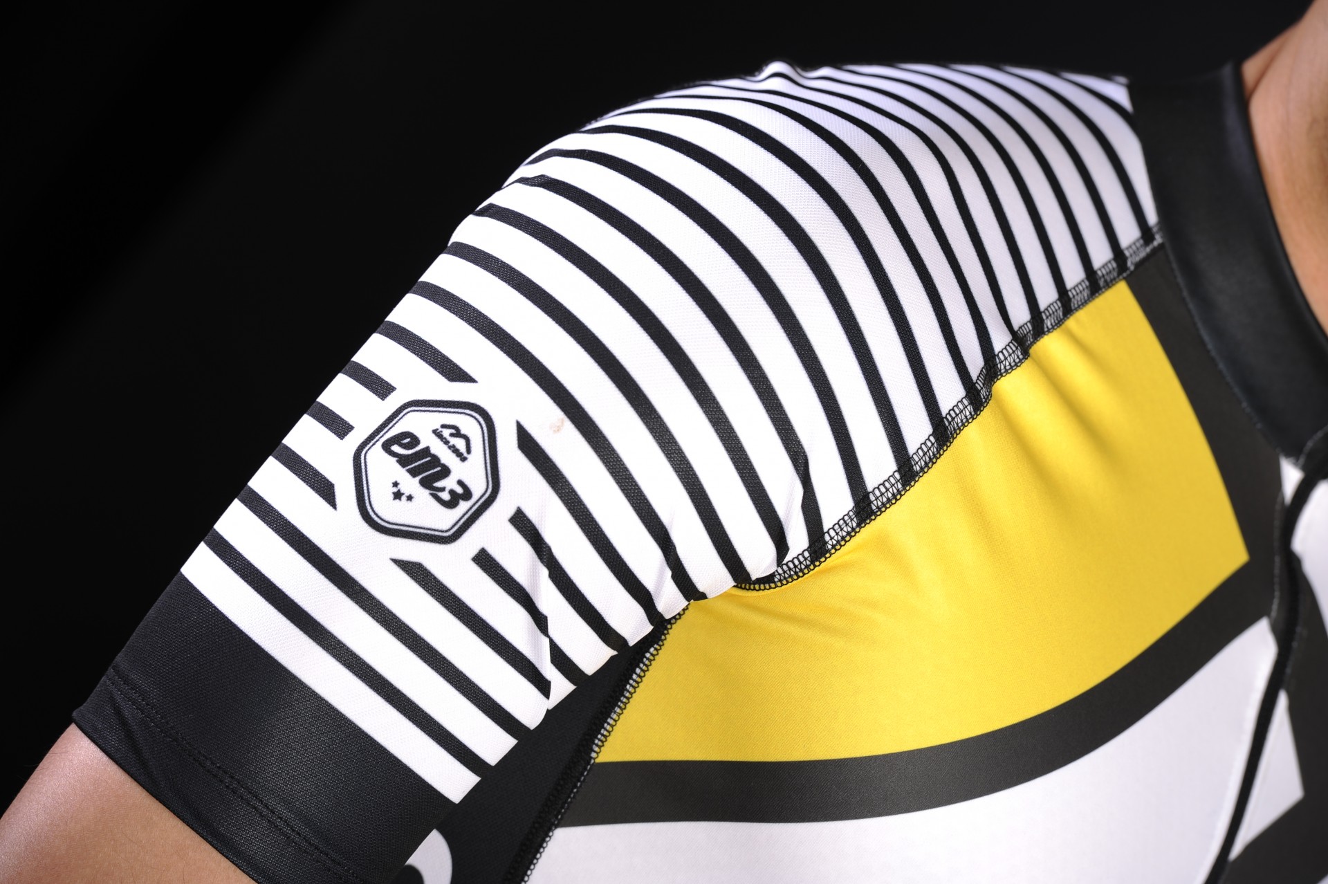 Camiseta desportiva com riscas pretas e brancas na manga e detalhes amarelos e pretos no corpo