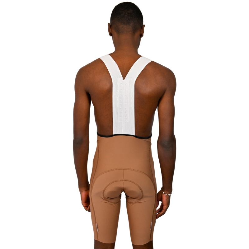 Calções ciclismo Pro Fit Creme Pessoa de costas com calções de ciclismo castanhos e alças brancas em fundo branco