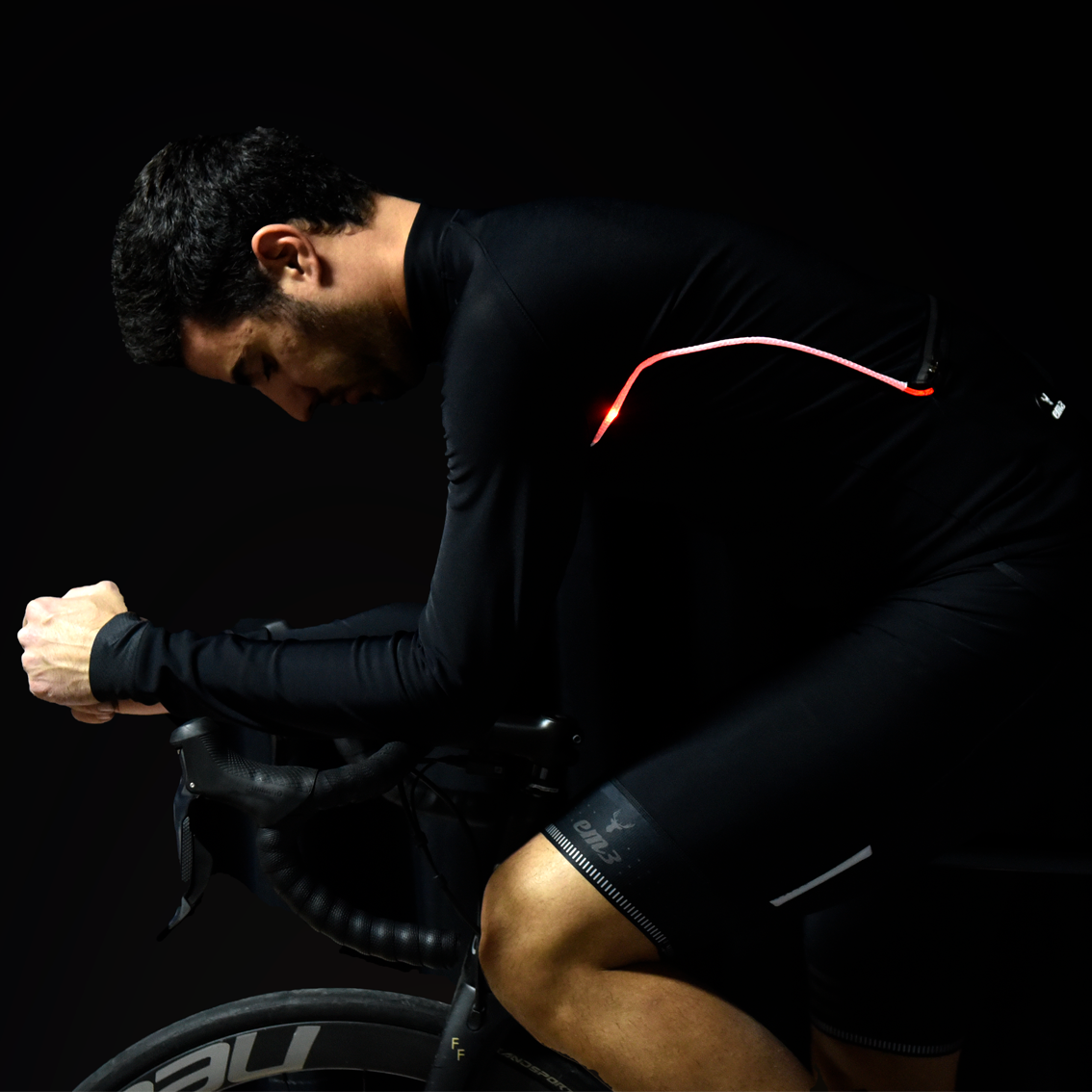 Casaco Ciclismo Led by OSRAM Ciclista de roupa preta com linha vermelha numa bicicleta de estrada preta