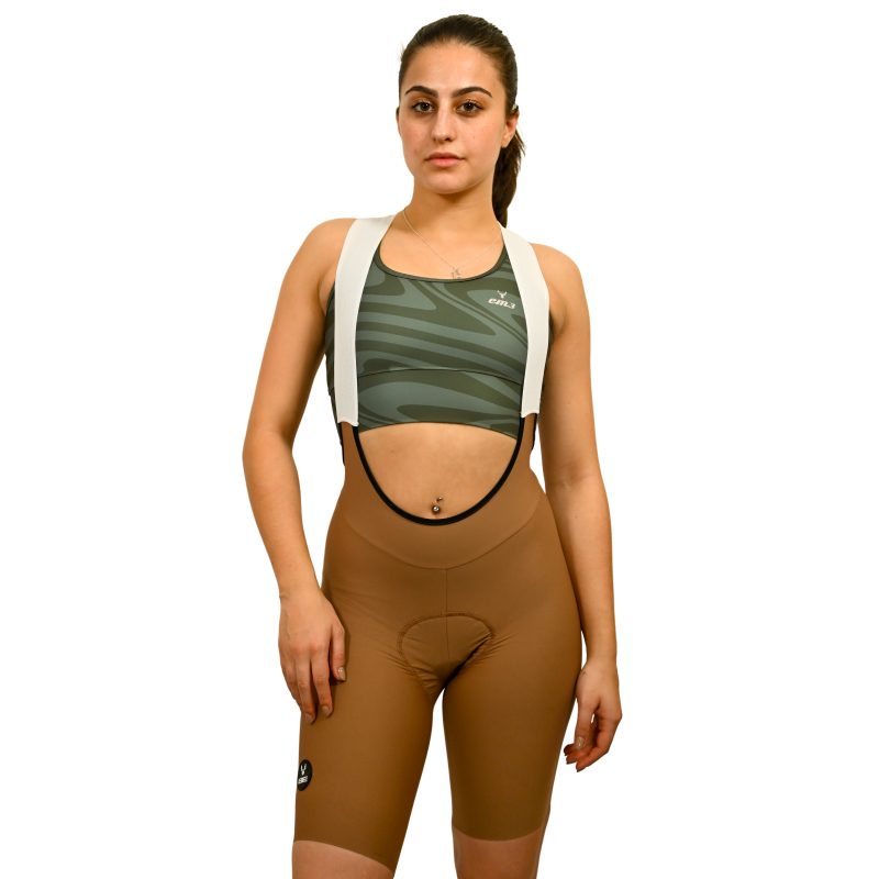 Calções ciclismo Pro Fit Creme Mulher com roupa desportiva: top verde zebrado e calção castanho com suspensórios brancos.