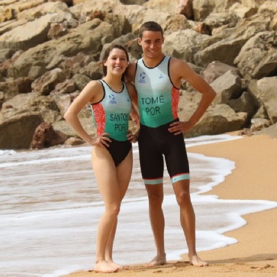 Dois jovens em fatos de triatlo pretos com inscrições verdes e vermelhas na praia