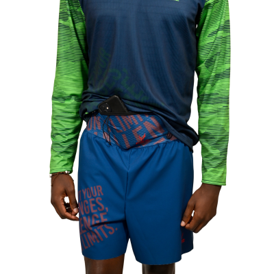 Pessoa com calção azul e camisola azul e verde, com telemóvel preto no cós.