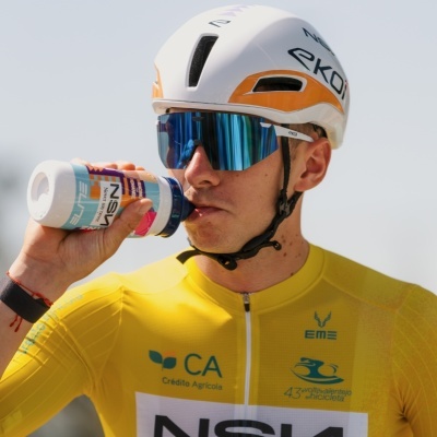 Ciclista a beber de bidão com capacete e óculos e camisola amarela de ciclismo