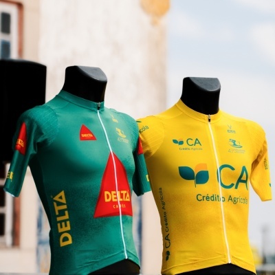 Dois fatos de ciclismo em manequins, um verde com logos DELTA e outro amarelo com logos CA Crédito Agrícola.
