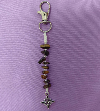 Porta-chaves com contas e pendente metálico sobre fundo lilás