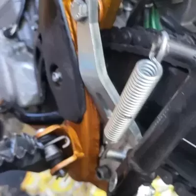 Peça metálica com mola em estrutura alaranjada e preta de motocicleta