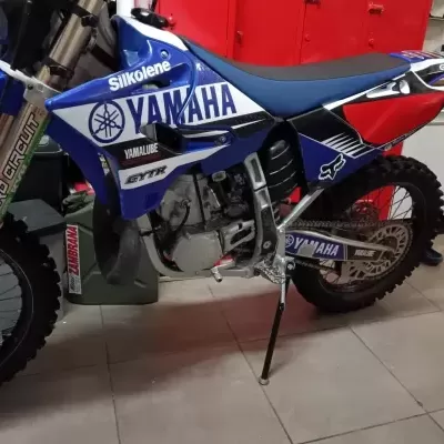 Motocross Yamaha azul, branco e vermelho com texto Silkolene, Yamalube, GYTR, GoldenTyre, Pro Circuit, Zambrana, motor exposto e suporte de descanso