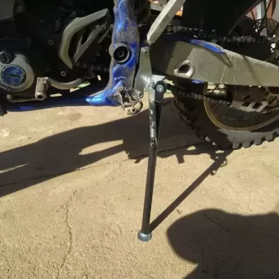 Descanso lateral de mota em metal prateado montado em mota azul sobre piso de cimento