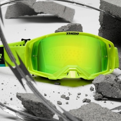 Óculos de proteção verde néon refletor marca THOR sobre destroços de cimento e arame farpado.