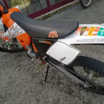 Motocross KTM 525 EXC laranja, branca e preta com decalques e autocolantes, punhos laranja, pneus de borracha, parada em pavimento pedra