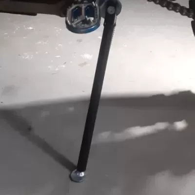 Parte inferior de moto verde com pedal de metal e suporte lateral no chão